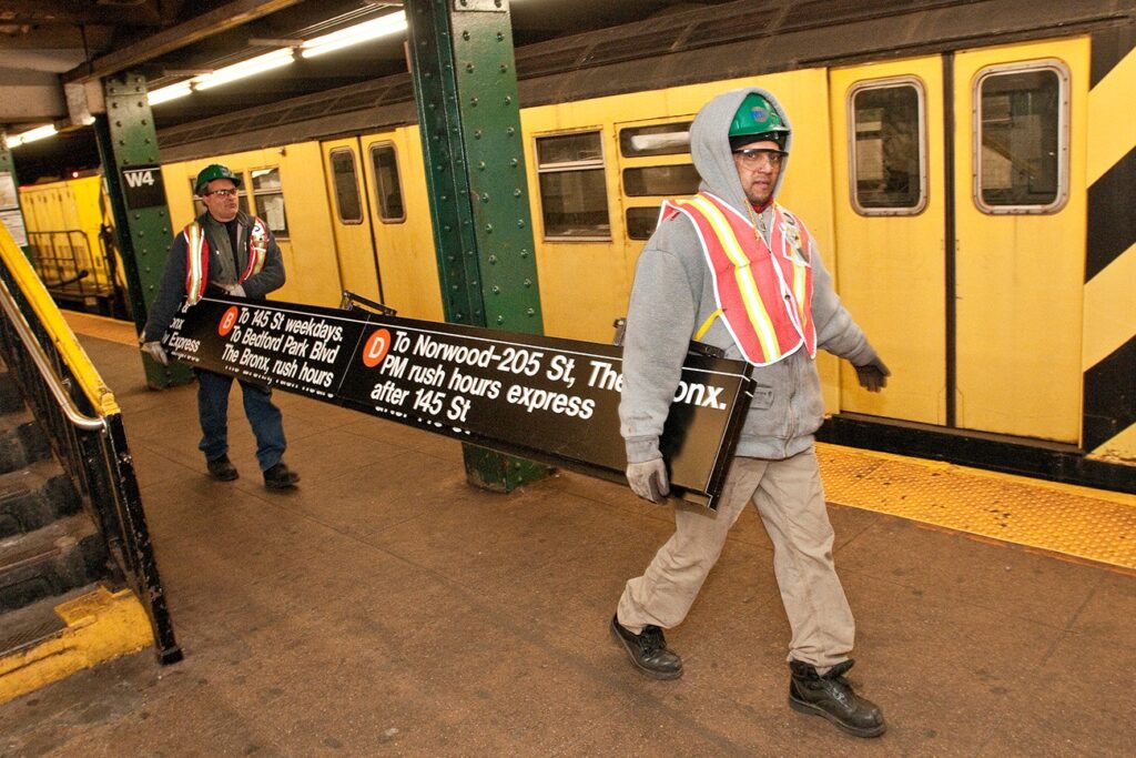 Workers moving a sign in a New York City subway station